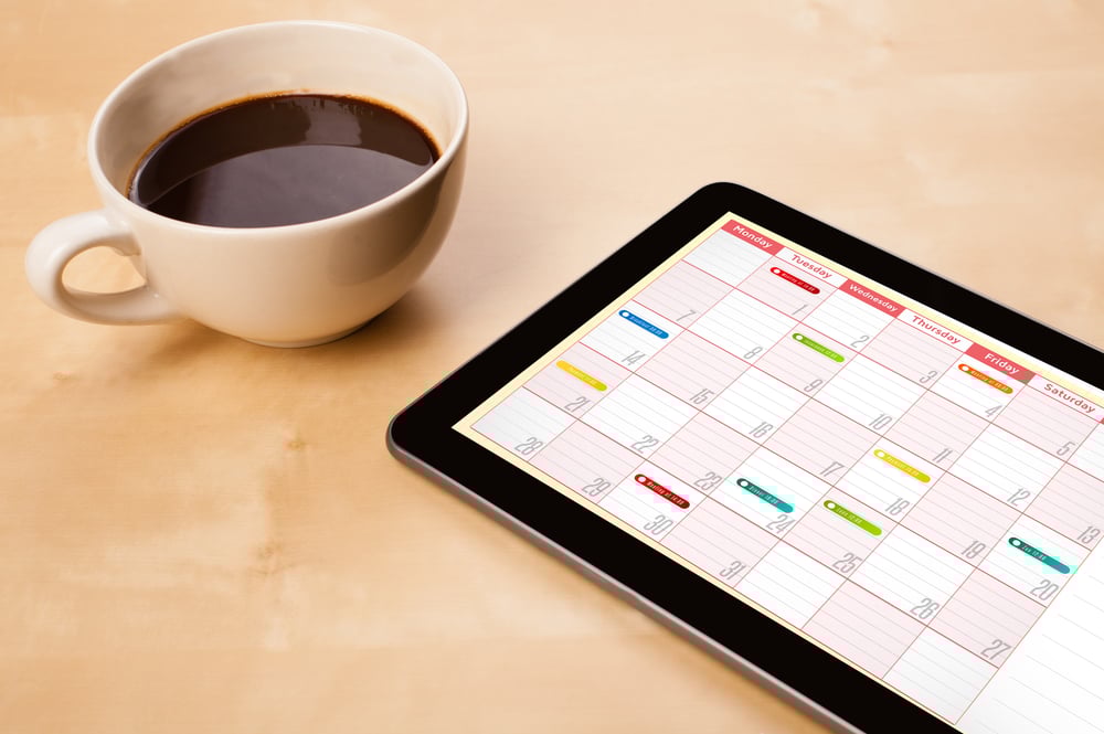 Workplace with tablet pc showing calendar and a cup of coffee on a wooden work table close-up Workplace with tablet pc showing calendar and a cup of coffee on a wooden work table close-up