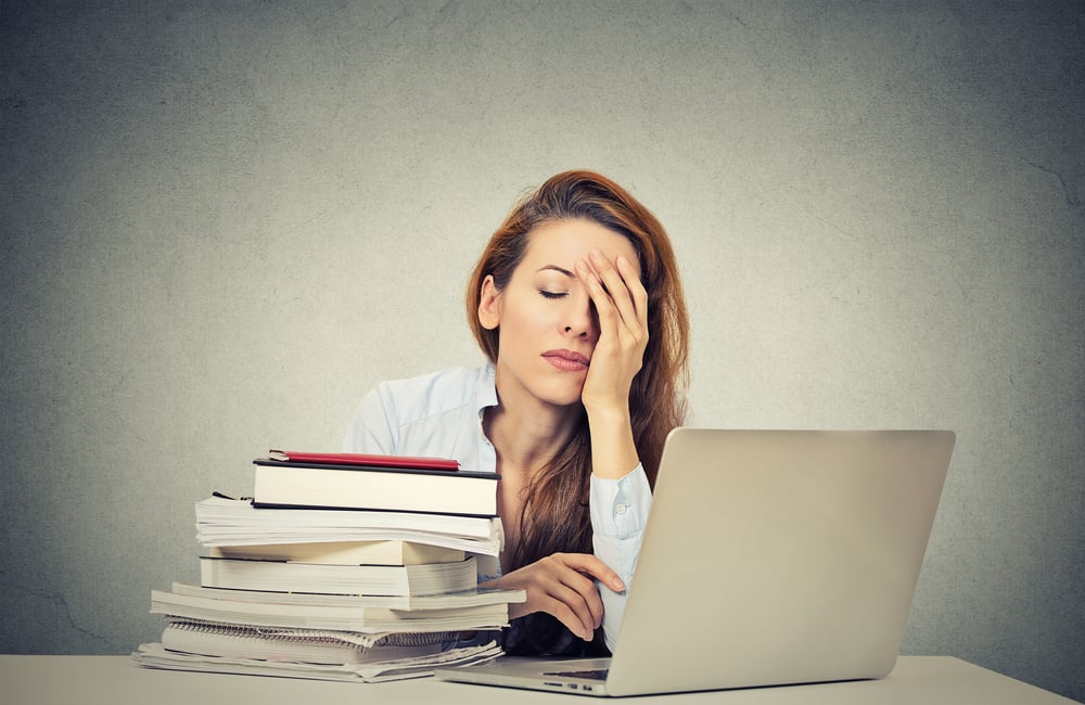 Too much work tired sleepy young woman sitting at her desk with books in front of laptop computer isolated grey wall office background. Busy schedule in college, workplace, sleep deprivation concept Too much work tired sleepy young woman sitting at her desk with books in front of laptop computer isolated grey wall office background. Busy schedule in college, workplace, sleep deprivation concept